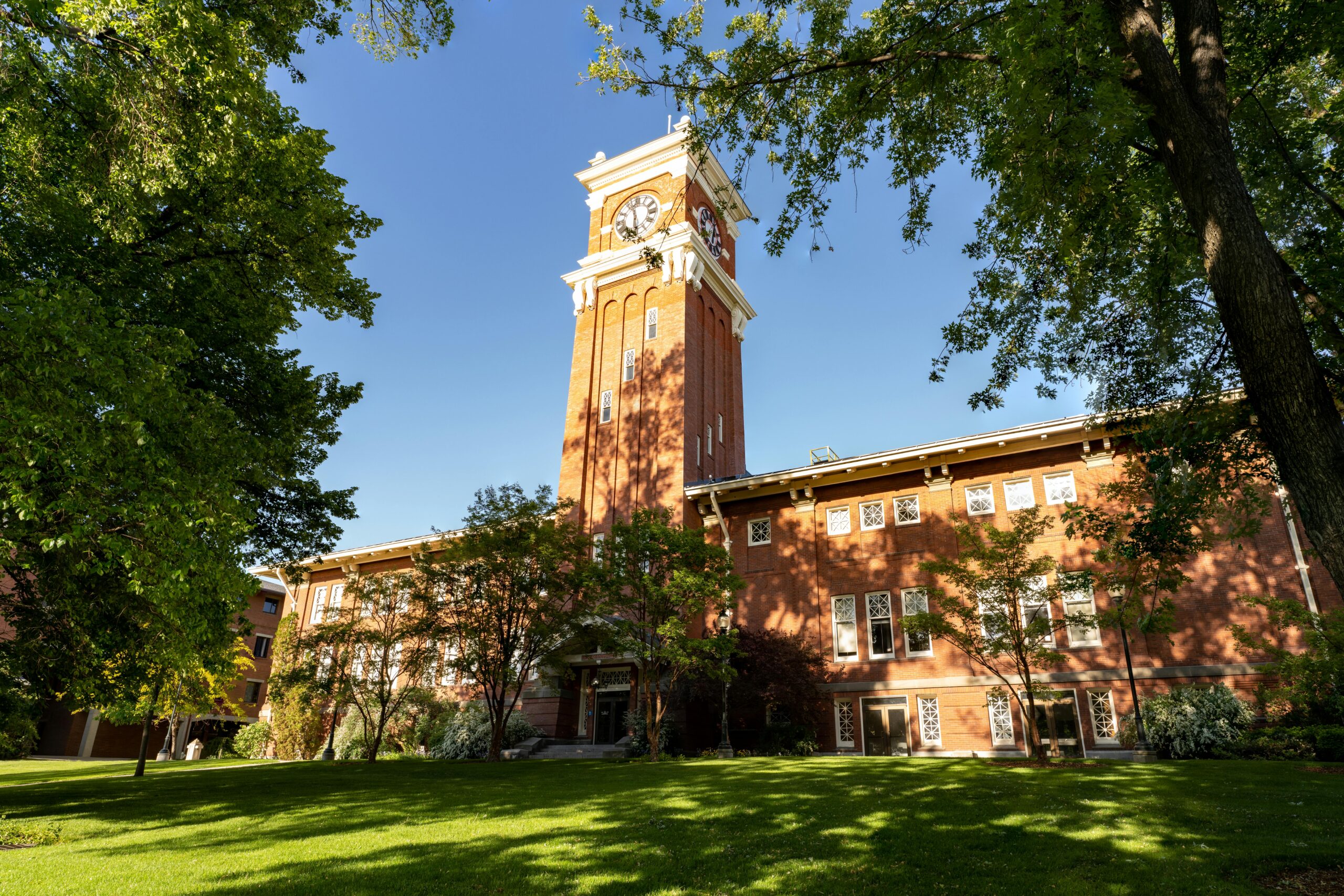 Beautiful view of the iconic clock tower at WSU under a clear blue sky, surrounded by lush greenery.